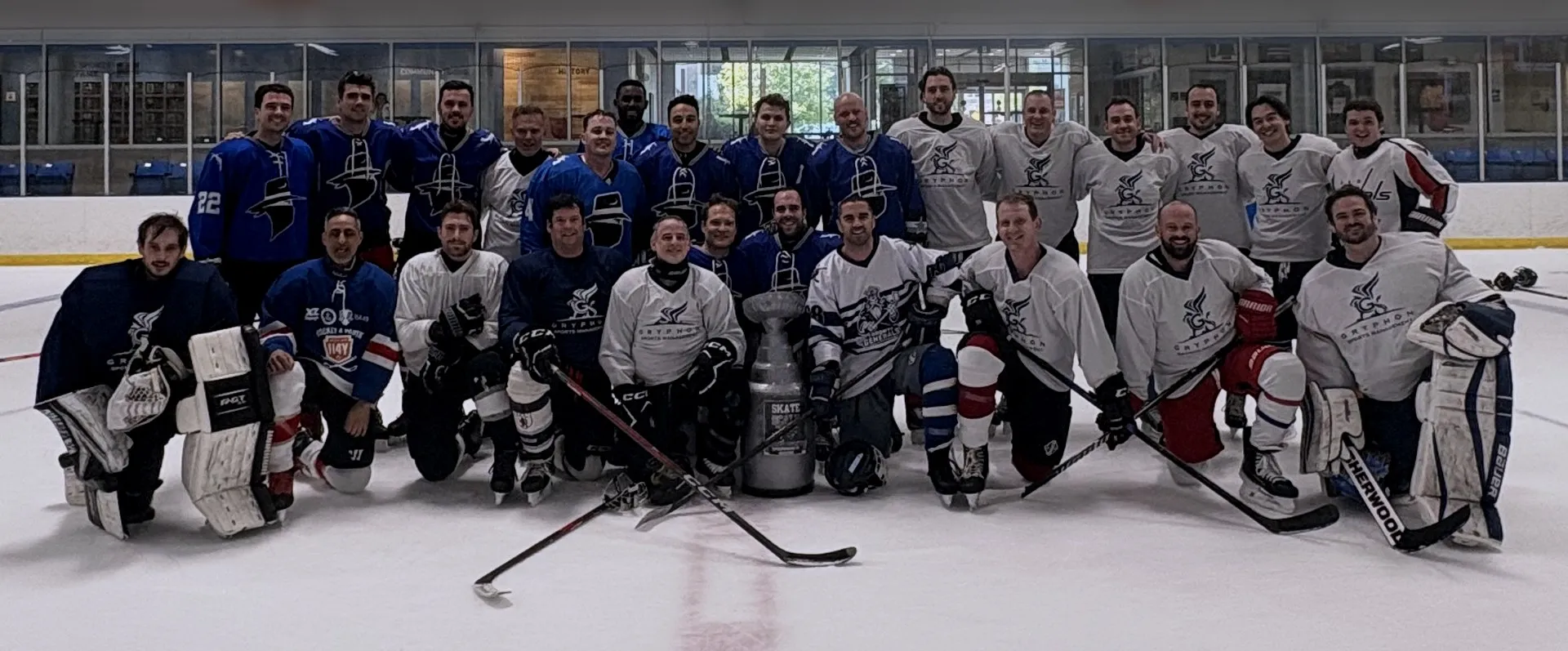 A large group of players in Gryphon Sports Management jerseys posing on the ice with a trophy