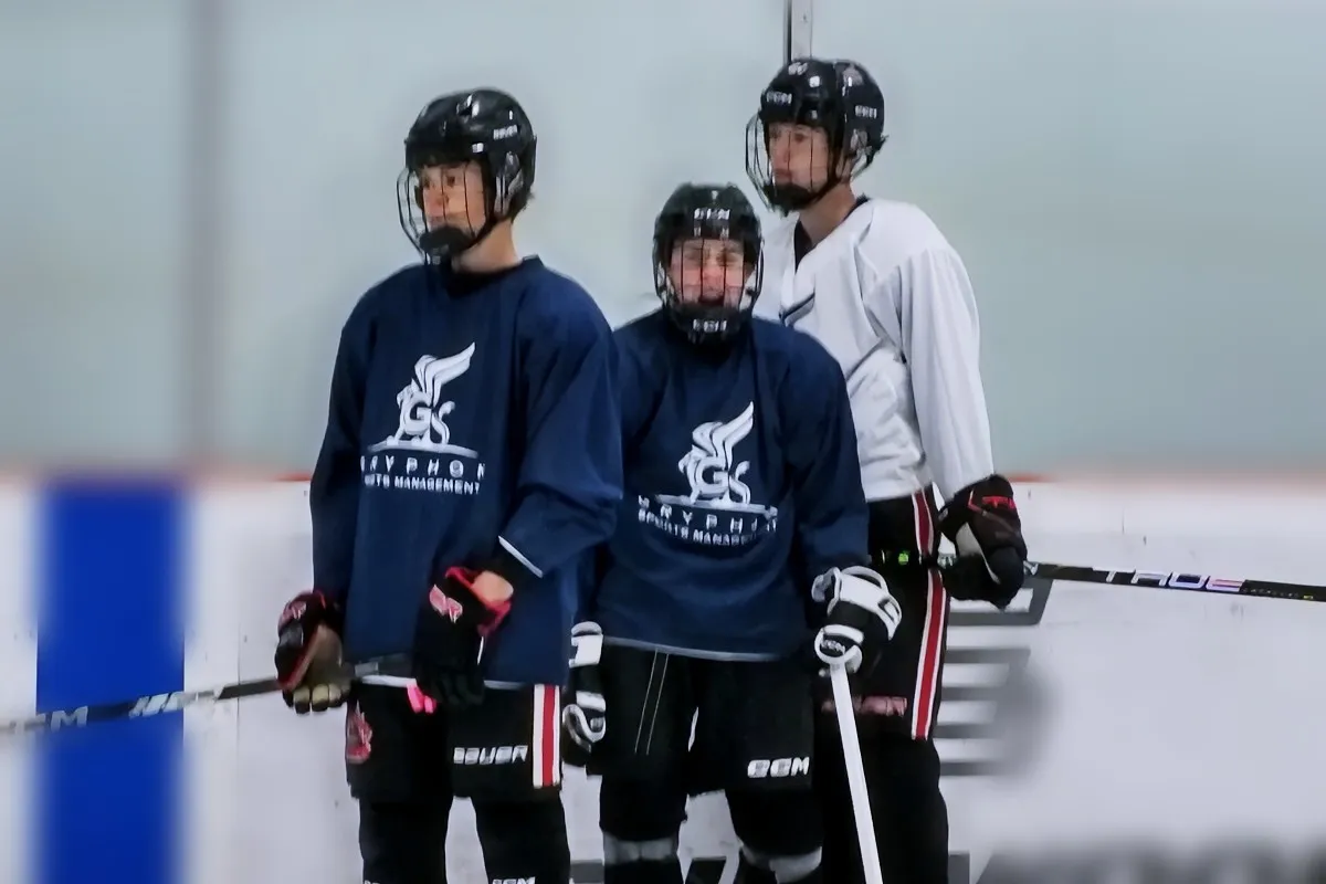Three players in Gryphon Sports Management jerseys standing along the boards